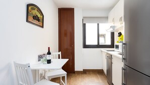 A compact kitchen with white cabinetry, a wooden door, and a dining area with a white table and chairs. - Piso Elegante y Luminoso (La Victoria de Acentejo)
