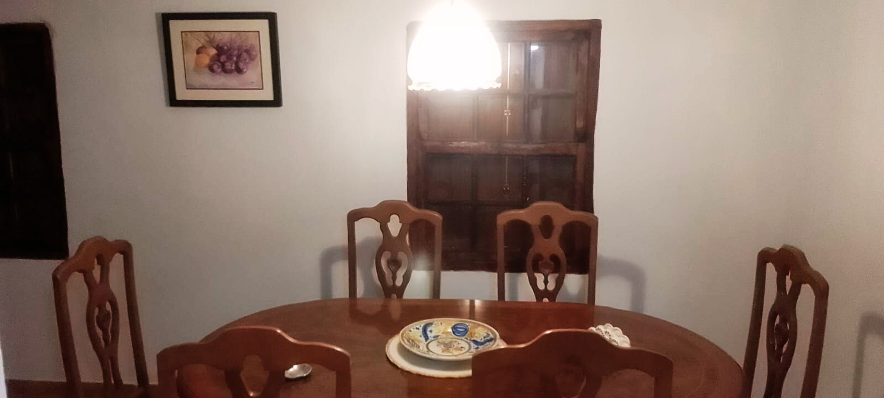 A dining area with a round wooden table, four chairs, and a plate with a decorative design.
