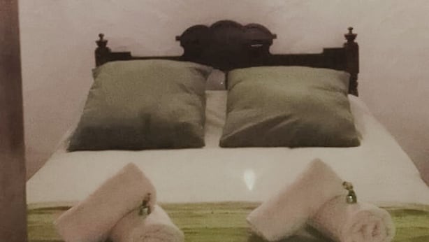 Un letto singolo con un poggiatesta, due cuscini e due asciugamani arrotolati.