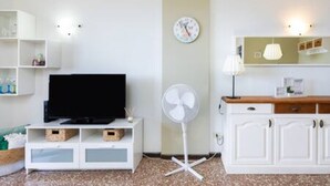 A modern living room with a flat-screen TV, a standing fan, a clock, and a cabinet with a mirror. - Apartamento Coral Sunsent View (Tacoronte)