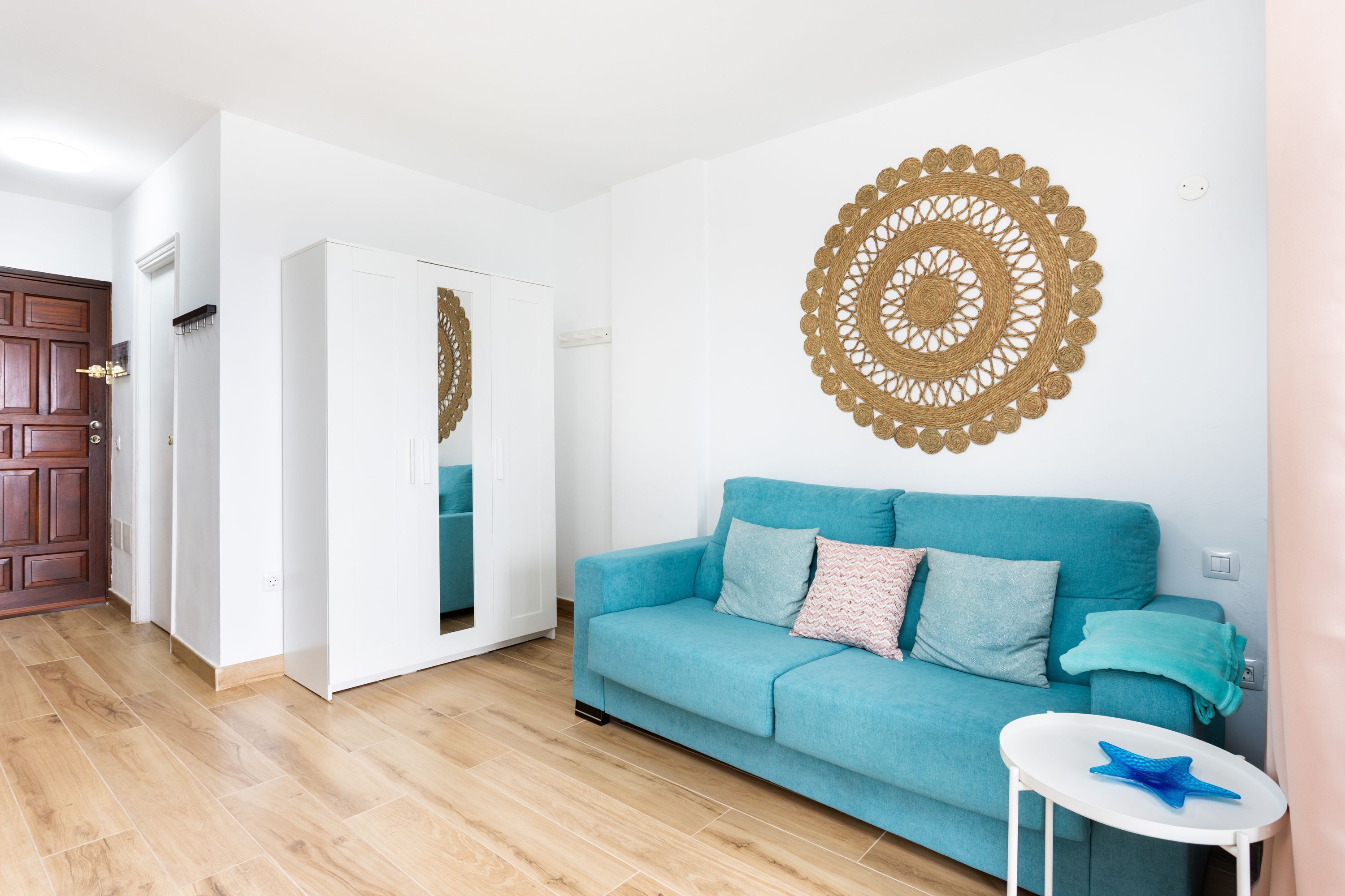 A living room with a teal sofa, a small white side table, and a large circular wall decoration.