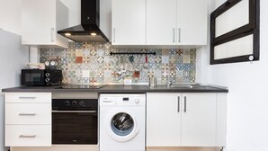 A compact kitchen with white cabinets, a Bosch washing machine, a microwave, and a patterned backsplash. - Brisa Marina (Tacoronte)