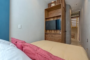 A bedroom with a bed, a wooden wardrobe, a flat-screen TV, and a door leading to a hallway. - Luxury Casita Calle 47 Gastronomic Corridor (Mérida)