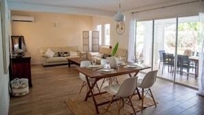 Un salon moderne avec un coin repas, comprenant un ensemble de canapés, une table à manger avec des chaises, un vase décoratif et une grande fenêtre donnant sur l’extérieur.