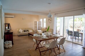 Ein modernes Wohnzimmer mit Essbereich, ausgestattet mit einer Sofagarnitur, einem Esstisch mit Stühlen, einer Dekovase und einem großen Fenster mit Blick ins Freie.