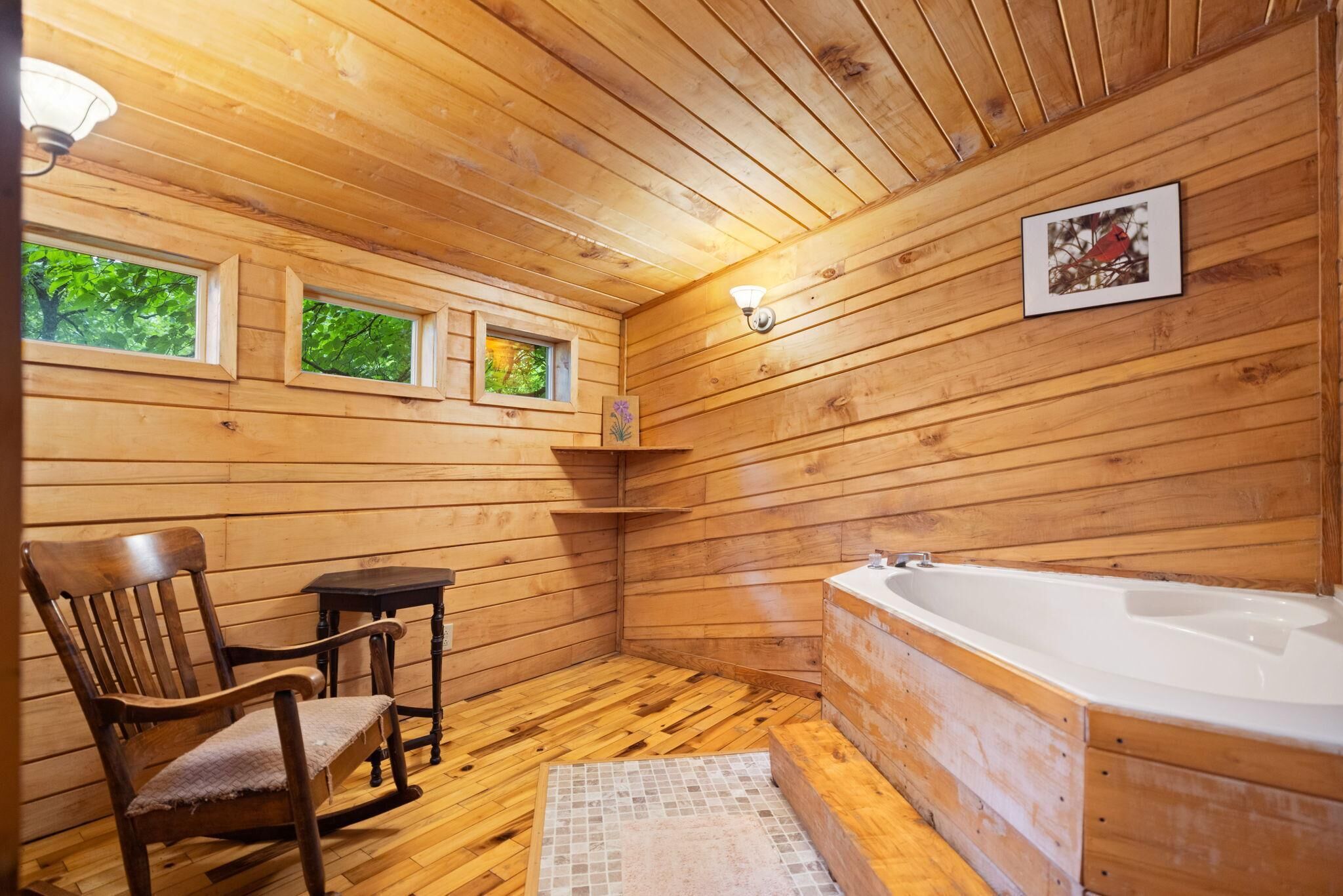 Ein Badezimmer einer Holzhütte mit Badewanne, einem Sessel, einem kleinen Tisch und einem Regal mit einem Bild.