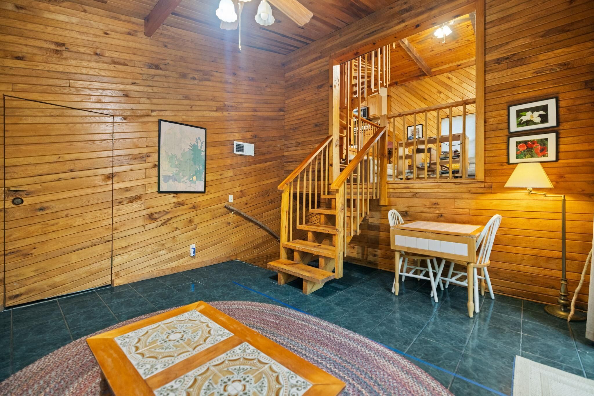 A wooden interior with a staircase, a dining area, and a rug.