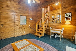 A wooden interior with a staircase, a dining area, and a rug.