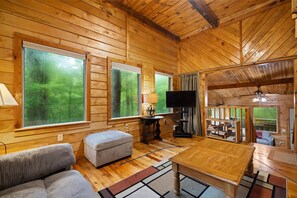 A cozy cabin interior with large windows, a television, a wooden table, and a sofa.