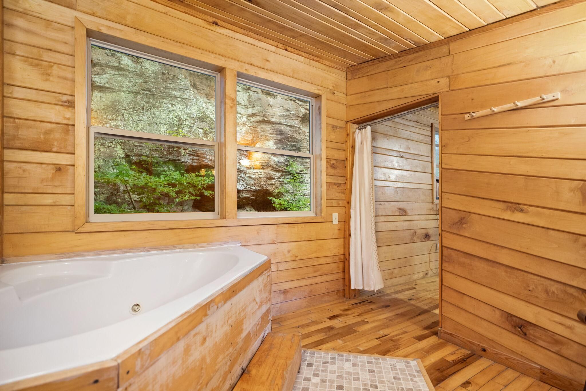 A wooden cabin bathroom with a bathtub, two windows, and a shower area.