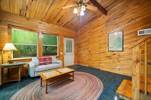 A wooden interior with a sofa, a coffee table, a lamp, and a large window.