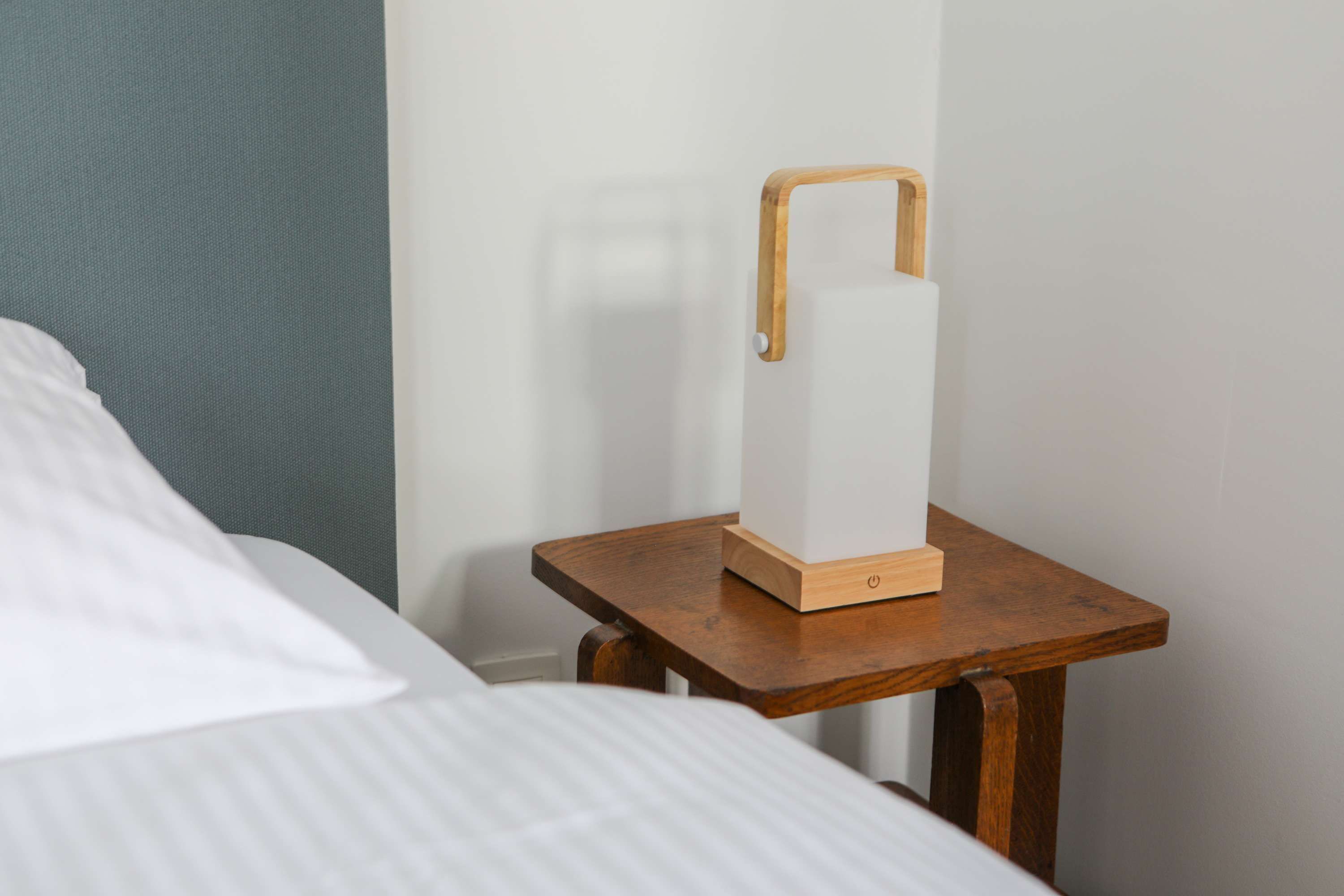 A bedside table with a white lamp and a wooden nightstand in a hotel room.