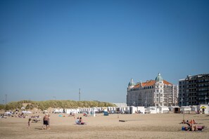 A beach with tents and umbrellas, a large building with a dome, and a sandy area with people. - Harbour View Stay - Stylish Apartment With Stunning Views in the Marina of Zeebrugge (Bruges)