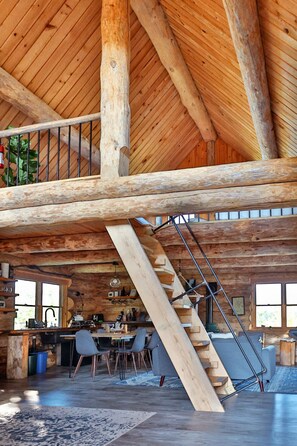 Un interior espacioso con un alto techo de madera, una escalera, una zona de cocina y un espacio para comer.