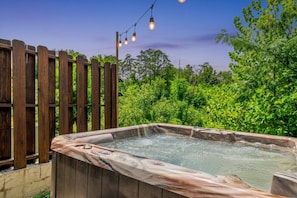 A hot tub with a wooden exterior, surrounded by greenery and a wooden fence.