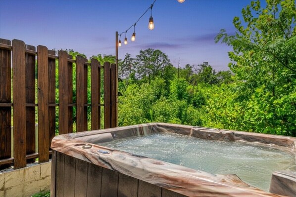Un jacuzzi con revestimiento de madera, rodeado de follaje y una valla de madera.