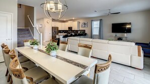 Una sala de estar moderna con comedor, muebles blancos, un televisor grande y un ventilador de techo.