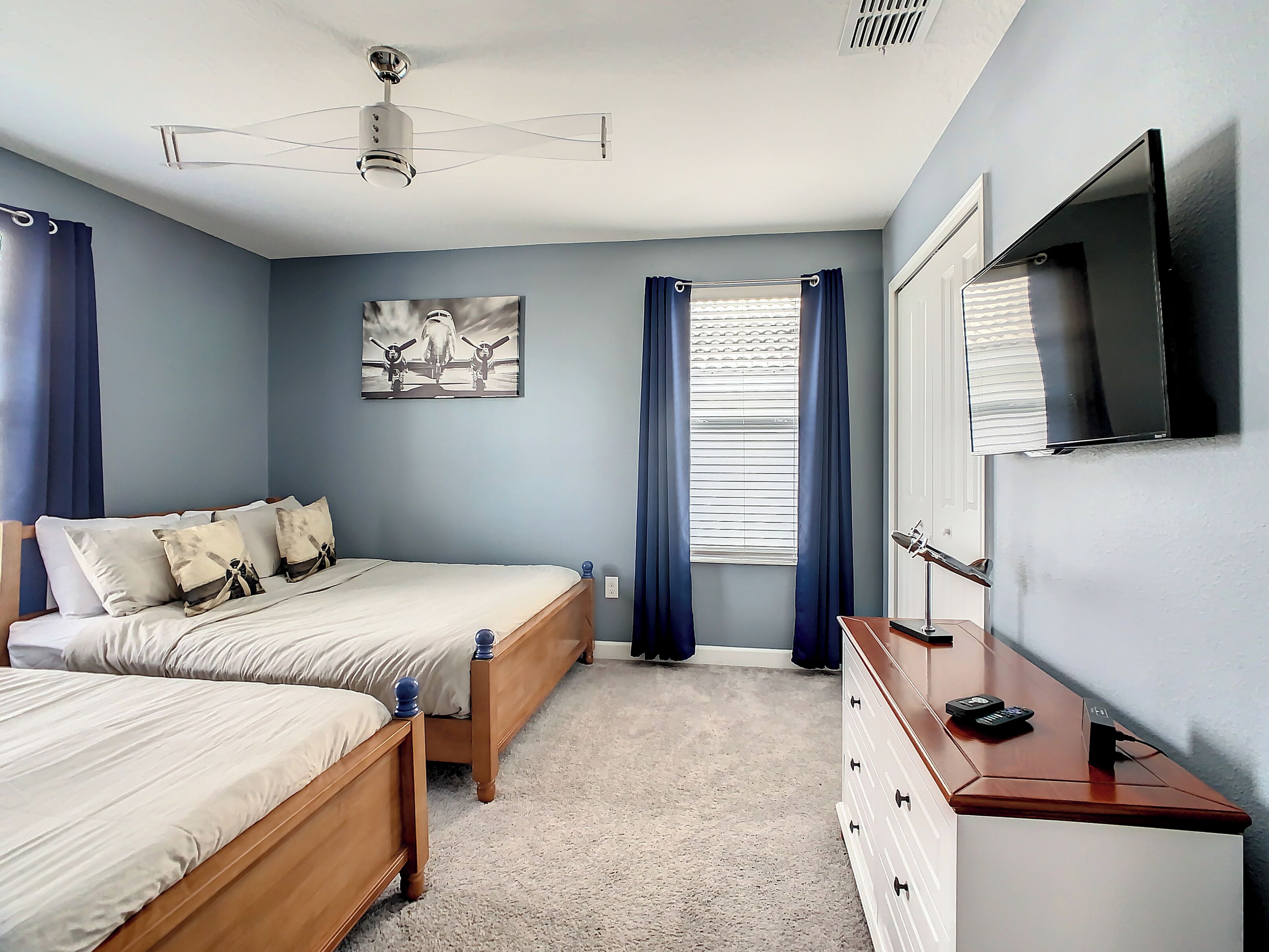 A bedroom with two beds, a ceiling fan, a flat-screen TV, and a window with curtains.