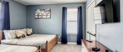 A bedroom with two beds, a ceiling fan, a flat-screen TV, and a window with curtains.