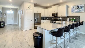 Una cocina moderna con gabinetes blancos, electrodomésticos de acero inoxidable y una isla central con taburetes de bar.