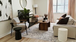 A modern living room with a sofa, armchair, coffee table, and a large abstract painting on the wall. - Charming Retreat in Raleigh, 2 bedrooms (Raleigh)