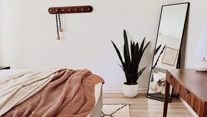 A bedroom with a bed, a bedside table, a desk, a potted plant, and a mirror. - Charming Retreat in Raleigh, 2 bedrooms (Raleigh)