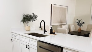 A modern kitchen with white cabinetry, a stainless steel dishwasher, and a black faucet. - Charming Retreat in Raleigh, 2 bedrooms (Raleigh)