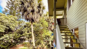 A wooden deck with a view of a lush garden and a building with a covered staircase.