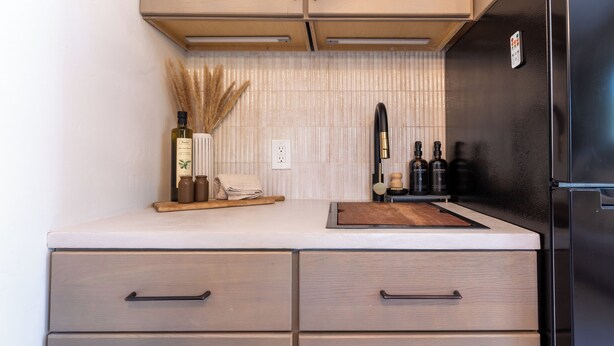 A modern kitchen with light wood cabinets, a white countertop, and a black refrigerator.