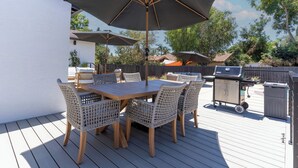 An outdoor patio with a wooden table and wicker chairs, a barbecue grill, and umbrellas.