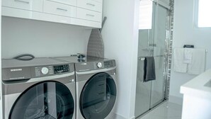 A modern bathroom with a glass shower enclosure, a built-in washing machine, and a white vanity.
