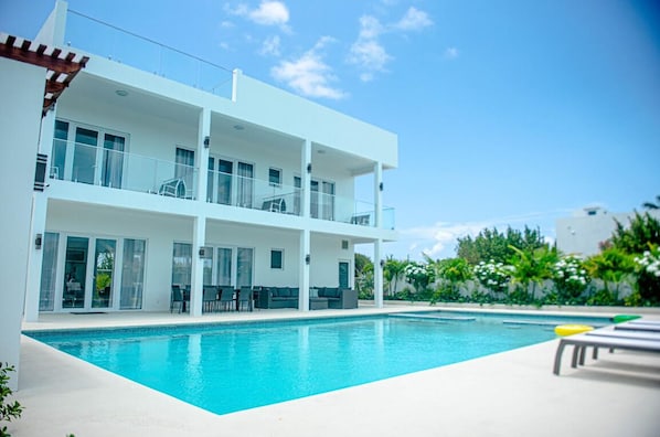 A modern two-story building with a swimming pool, outdoor seating, and a clear blue sky.