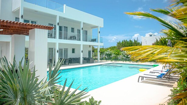 A modern two-story building with a swimming pool, outdoor seating, and lush greenery.