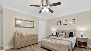 A bedroom with a bed, bedside tables, a dresser, a ceiling fan, and framed pictures on the wall.
