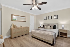 Une chambre à coucher comprenant un lit, des tables de chevet, une commode, un ventilateur de plafond et des tableaux encadrés accrochés au mur.