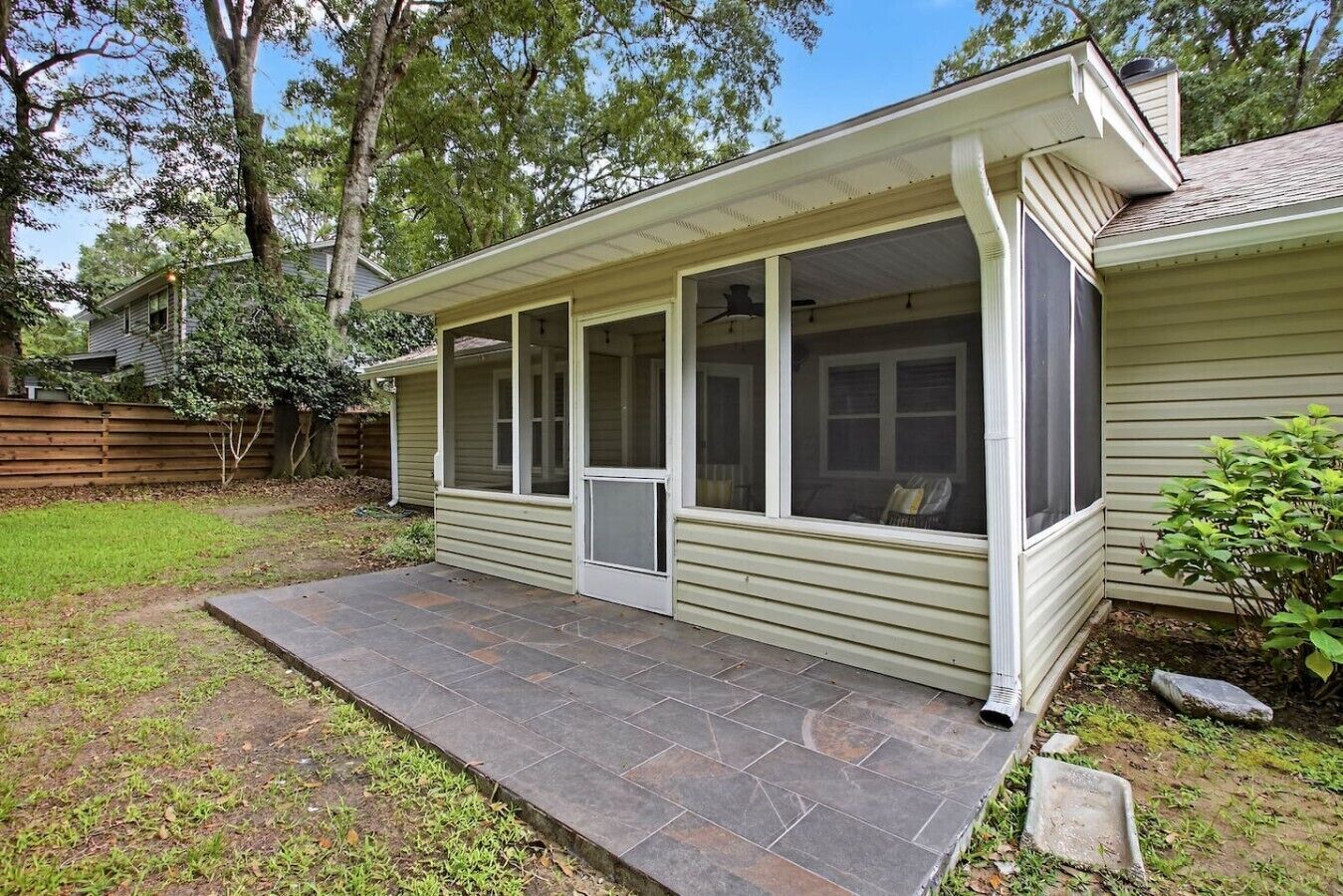 A house with a covered porch, a stone patio, and a fenced backyard.