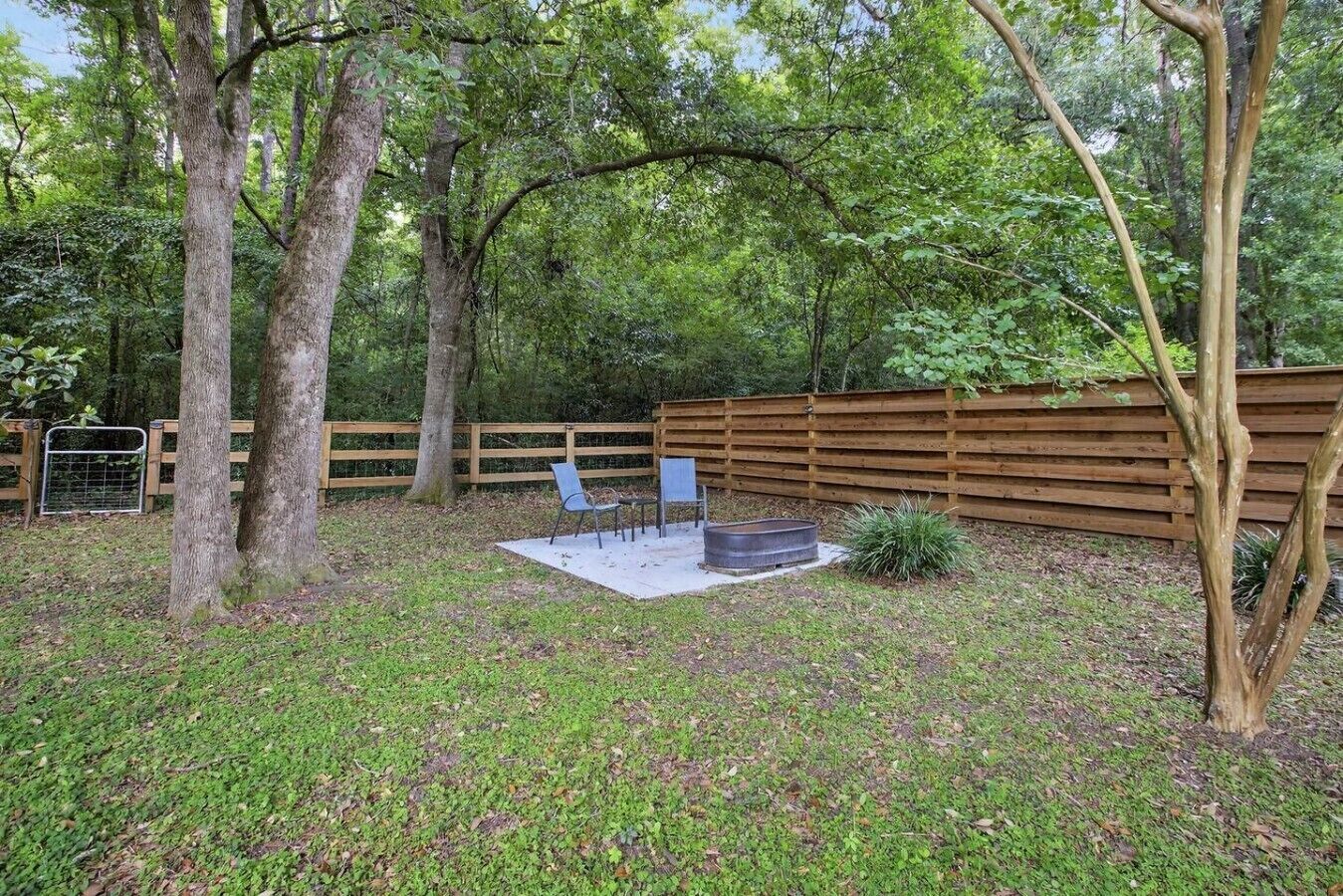 A backyard with a wooden fence, a fire pit, and two chairs.