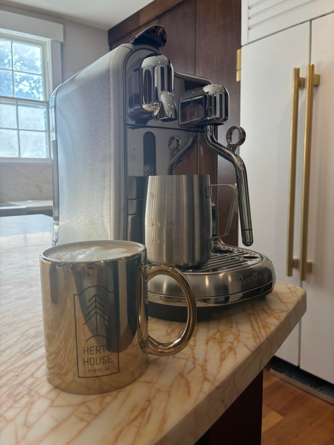 A Breville coffee maker on a marble countertop with a stainless steel mug labeled "Hert House Athens, GA".