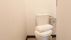 A small, clean bathroom with a white toilet, a white towel on the seat, and a white rug on the floor. - Airport Manini Lodge Studio 5 (Faaa)