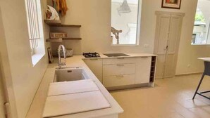 A modern kitchen with a central island, a window, and a door. - Le Ficus Grande Villa Bord de mer Avec Piscine (Paea)
