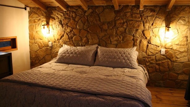 Een bed met een gewatteerd hoofdbord, een stenen muur en twee wandlampen.
