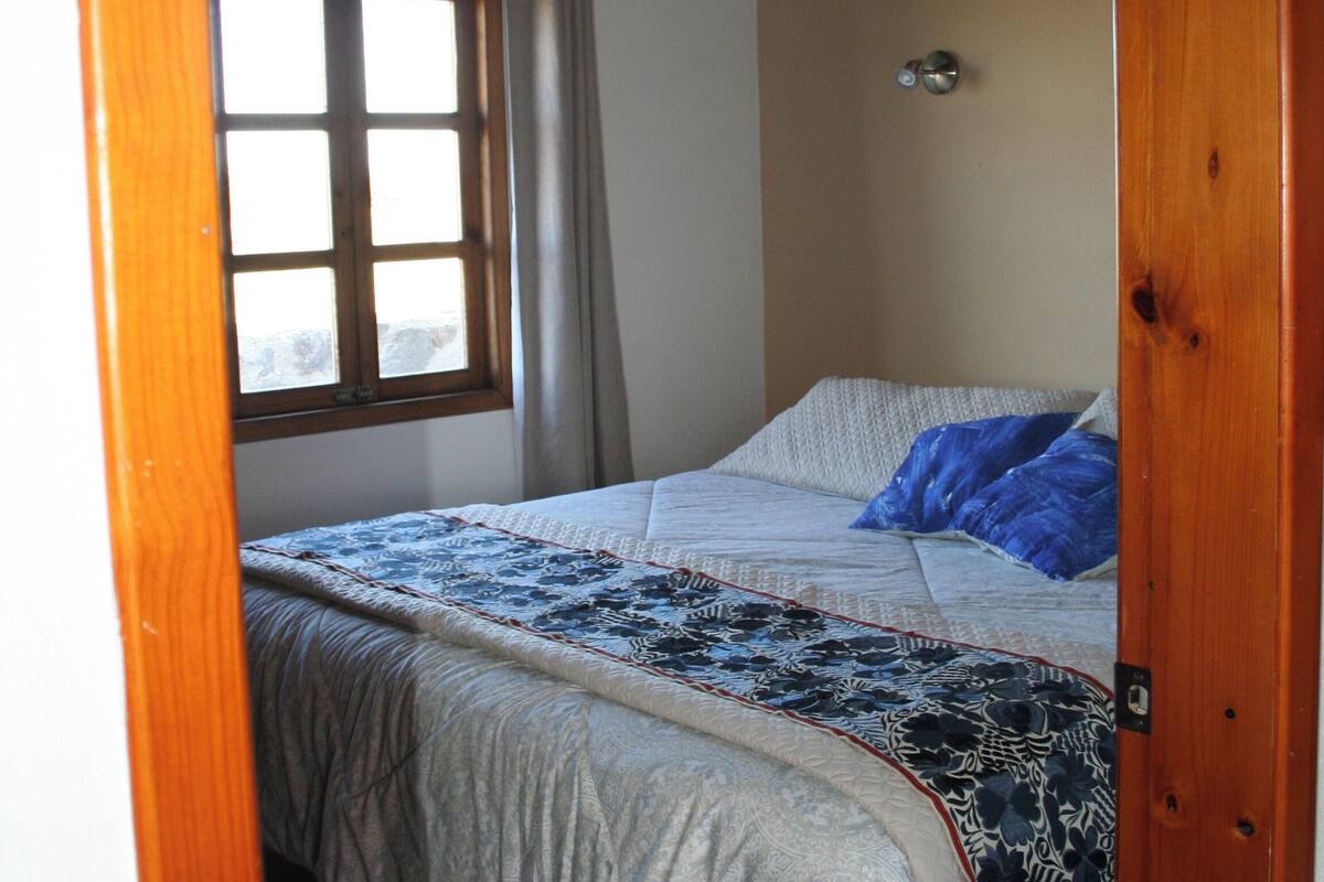 Un dormitorio con cama, ventana y techo de madera.