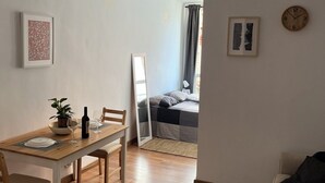 Een woonkamer met een bank, een eettafel met stoelen, een plant en een wijnfles.