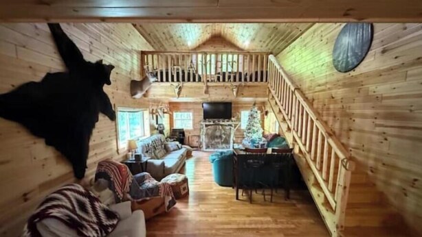 Interior de una cabaña de madera con un dormitorio en el altillo, una sala de estar con un sofá y televisión, y un comedor.