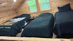Una cabaña con dos camas, paredes de madera y una ventana con vista a la vegetación.