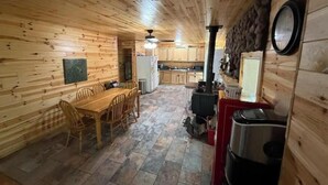 Interior de una cabaña de madera con comedor, cocina y estufa de leña.