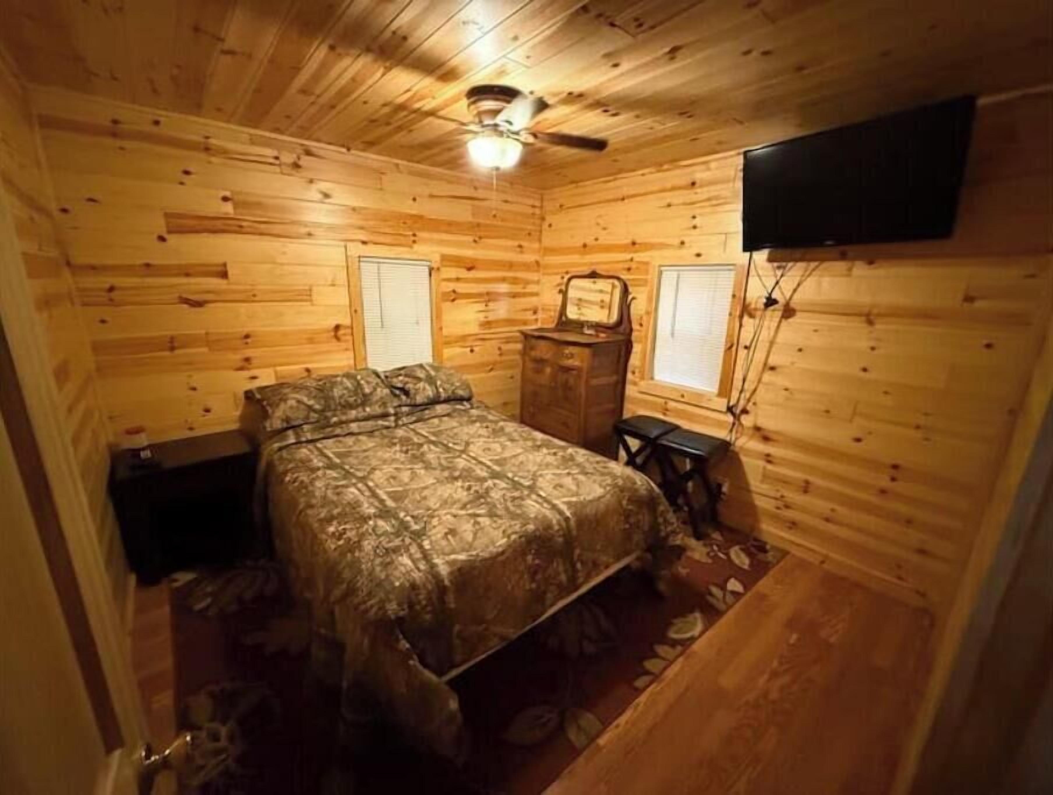 Een houten slaapkamer met een bed, een kaptafel, een dressoir en een plafondventilator.