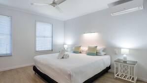 A bedroom with a bed, two bedside lamps, a ceiling fan, and an air conditioning unit.