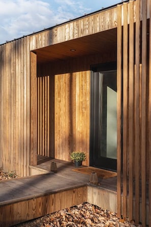 A modern building with vertical wooden panels, a central window, and a small outdoor seating area. - The Ridge at Serà - Modern Retreat w/Sauna (Wardensville)