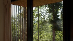 A bedroom with a large bed, a view of trees through a window, and a balcony with a metal railing. - The Ridge at Serà - Modern Retreat w/Sauna (Wardensville)